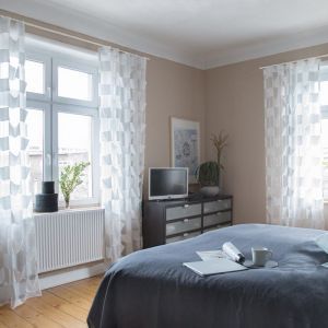 Schlafzimmer mit dunklen Möbeln und weißen gemusterten Vorhängen