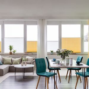 Helles Wohnzimmer mit türkisfarbenen Akzenten und gelben sowie weißen Vorhängen und Rollos