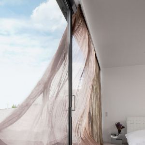 Beige-brauner Vorhang der aus dem Fenster weht