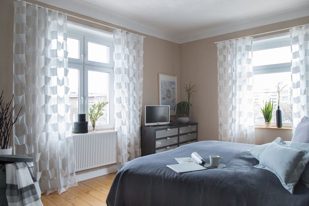 Schlafzimmer mit einem Bett, einem Fernseher und einem Fenster, das Tageslicht hereinlässt.